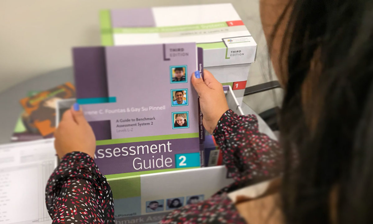 A person holding an Assessment Guide from the Benchmark Assessment System kit.