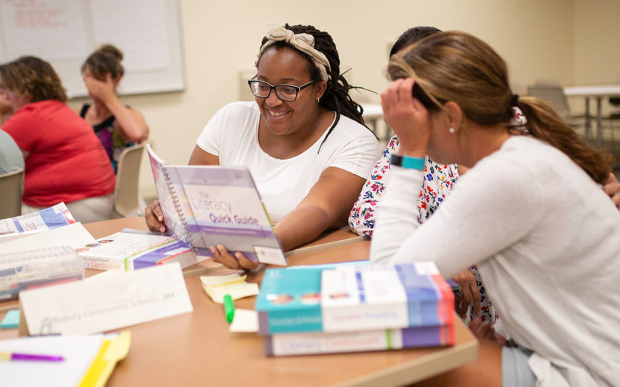 Three educators sitting at a table looking at a book together.