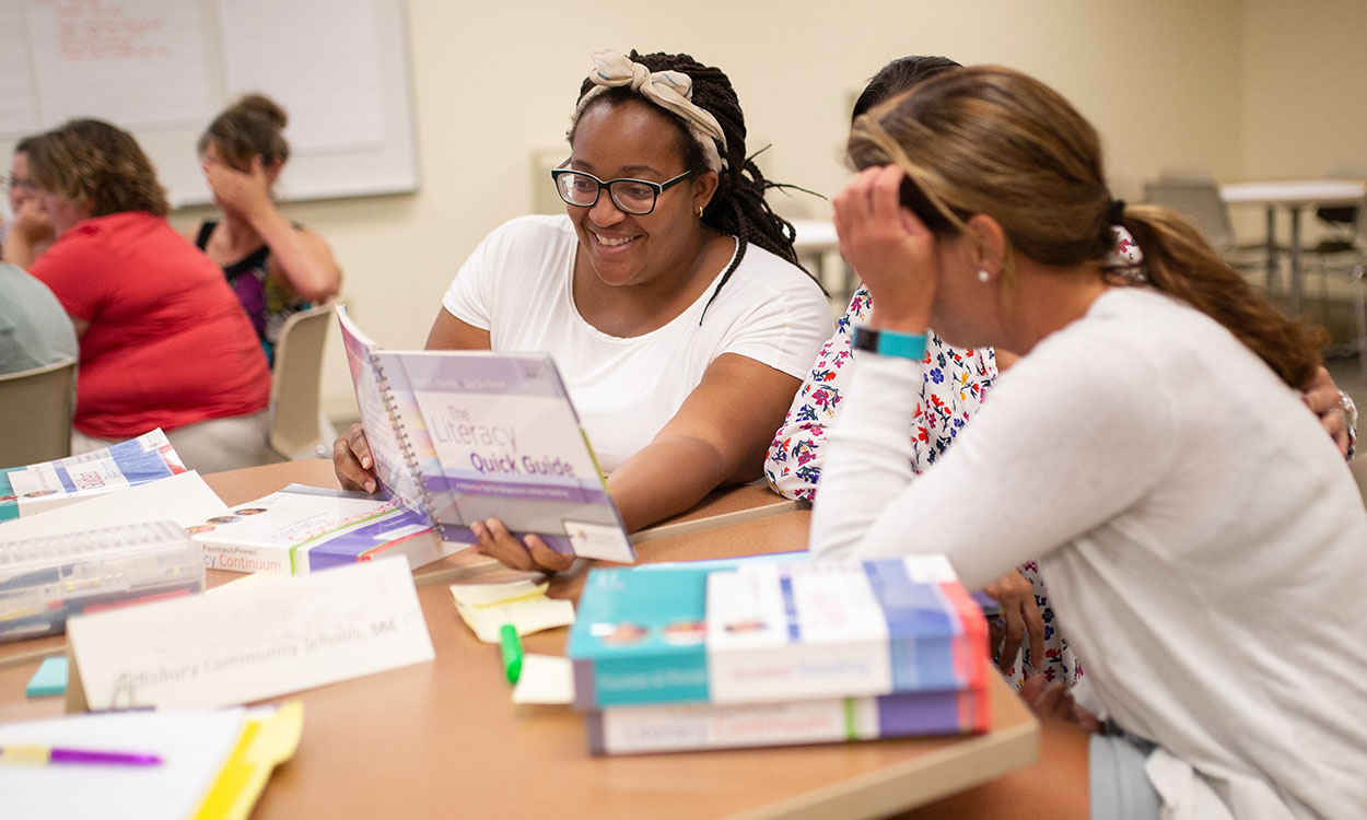 Three educators sitting at a table looking at a book together.