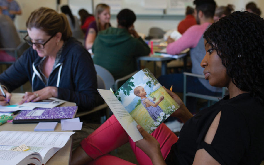 Educator sitting a table, looking through a children's book.
