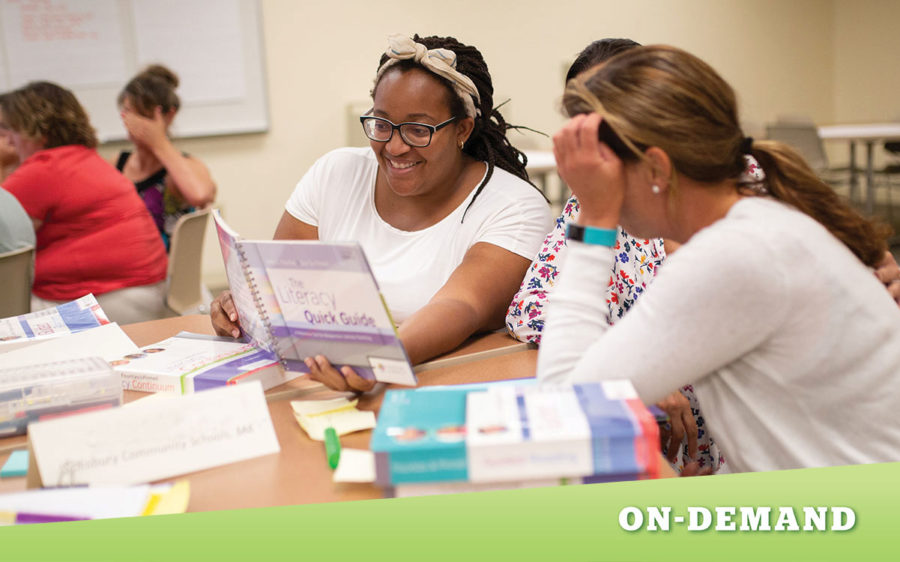 Three teachers sitting at a table, looking at a book together.