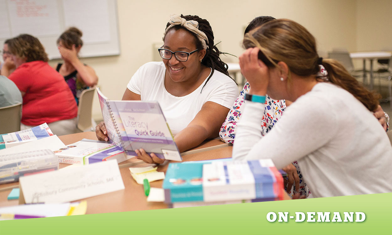 Three teachers sitting at a table, looking at a book together.