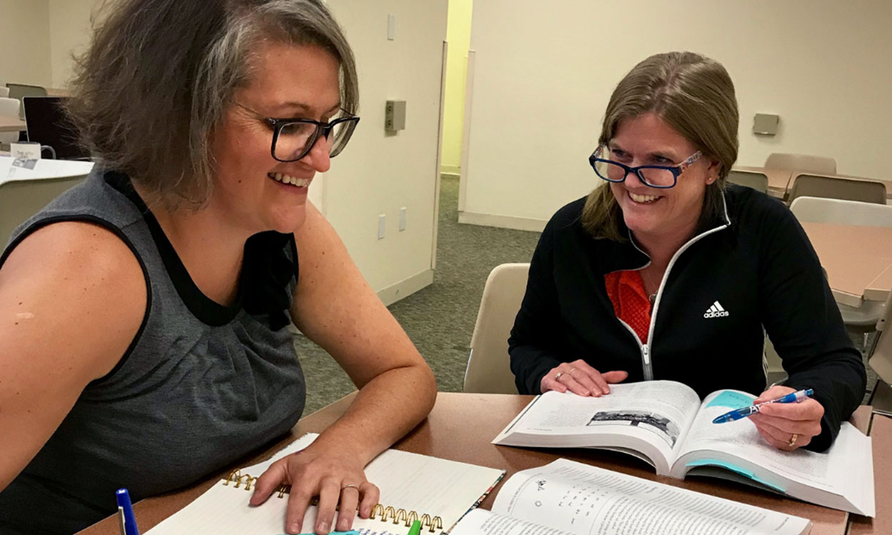 Two smiling educators sitting at a table together.