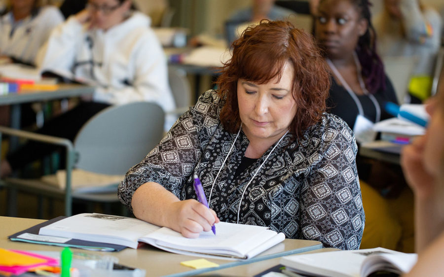 Educator sitting at table writing in a notebook.