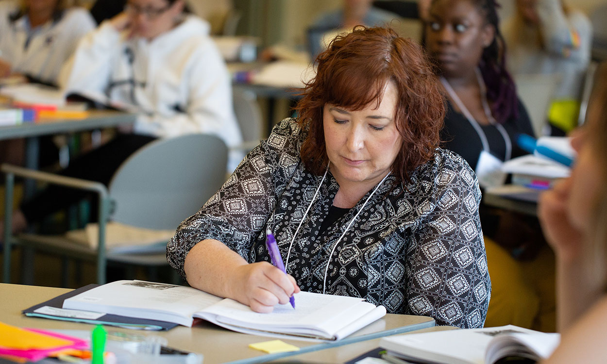 Educator sitting at table writing in a notebook.