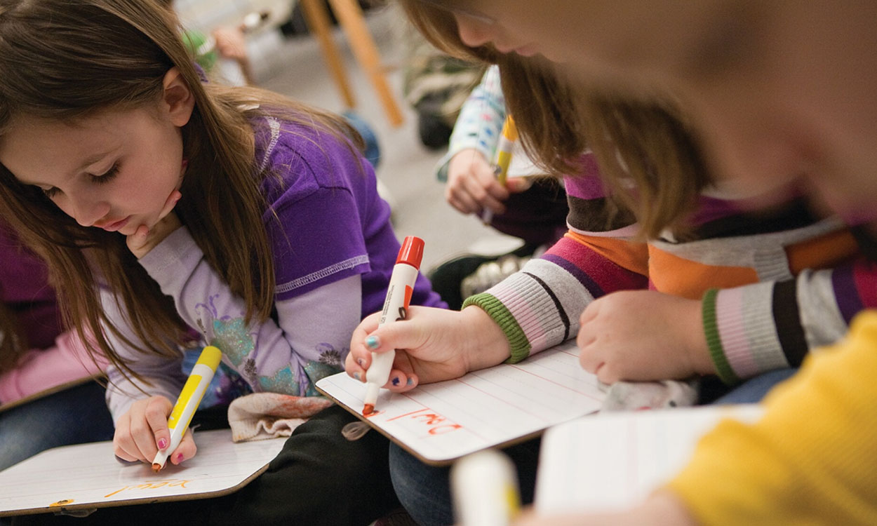 Children looking down, writing on individual whiteboards.