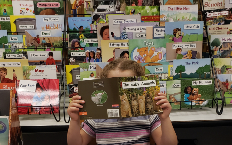 Child reading a book with leveled texts in the background.